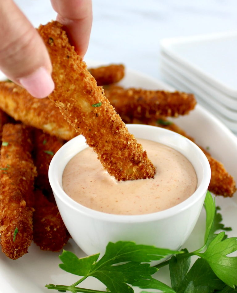 holding Halloumi Fry dipping into zesty dipping sauce in white bowl