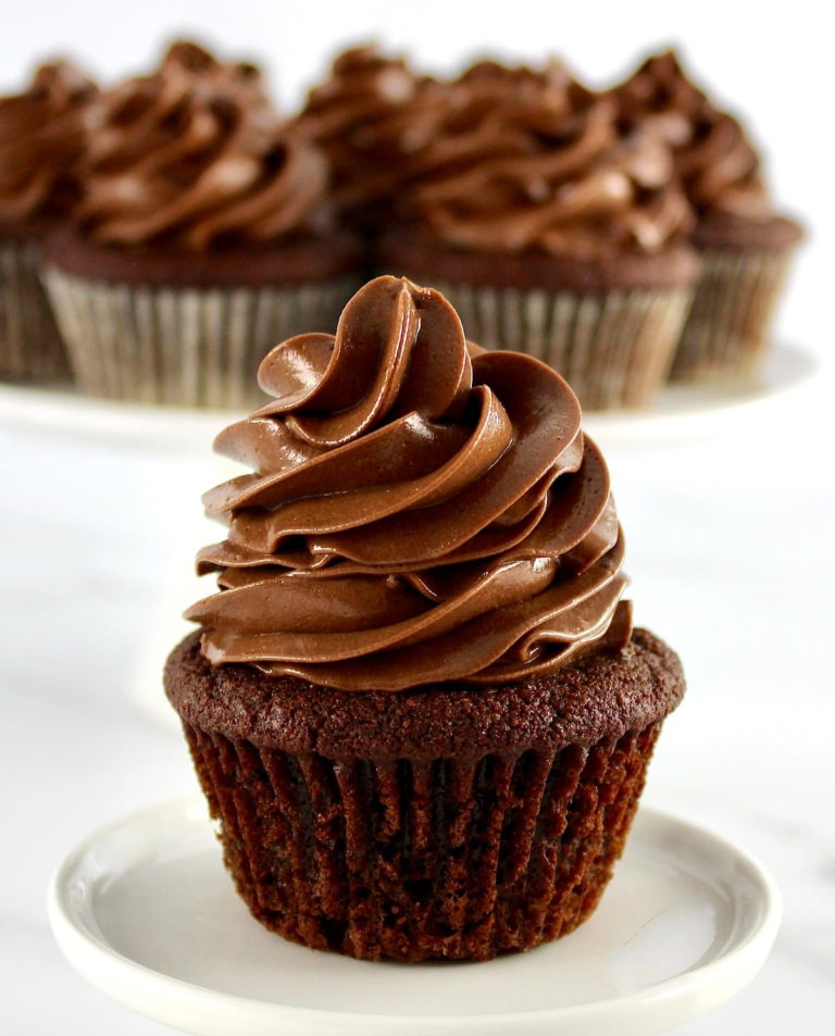 closeup of Keto Chocolate Cupcake on white round plate with more cupcakes in back
