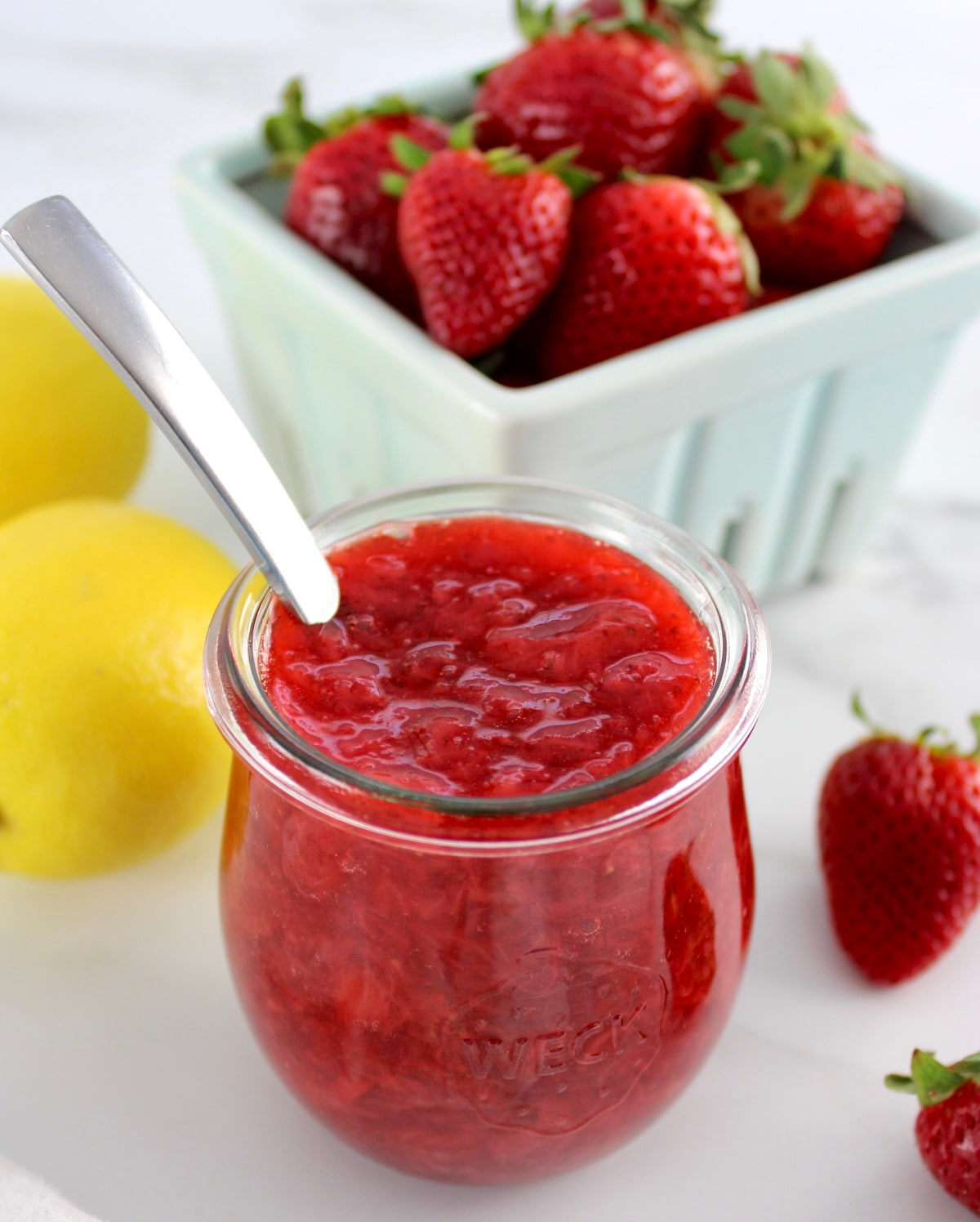 Keto Strawberry Sauce in open glass jar with spoon and strawberries in back