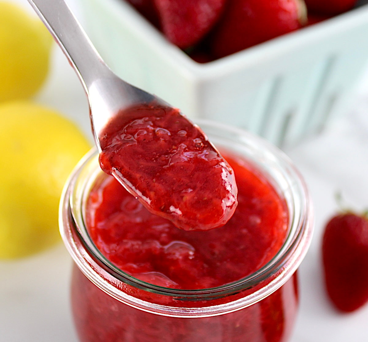 closeup of Keto Strawberry Sauce held up in spoon over open glass jar