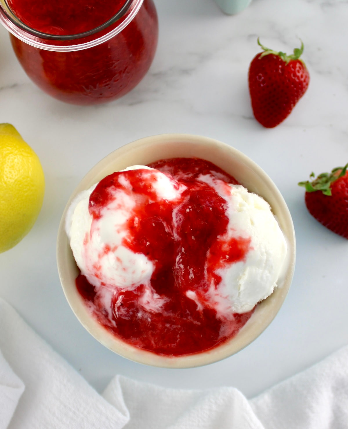 overhead view of vanilla ice cream in bowl with Keto Strawberry Sauce on top and more in back