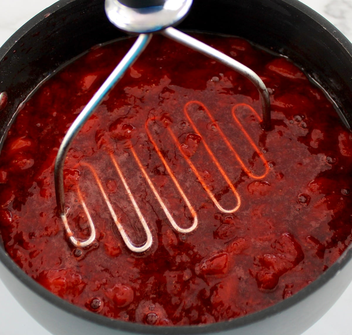 Keto Strawberry Sauce in saucepan with masher