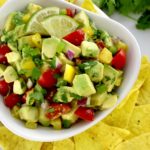 Avocado Salsa in white bowl with yellow tortilla chips around