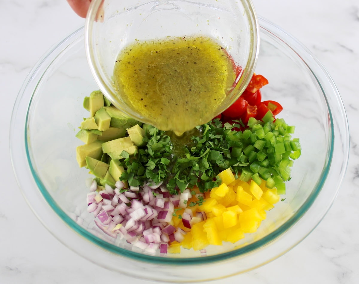 Avocado Salsa ingredients in glass bowl in groups with dressing pouring over top