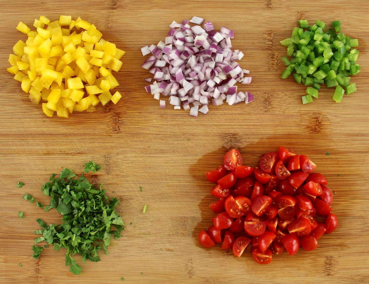 chopped peppers, onion, tomatoes and cilantro on cutting board in bunches