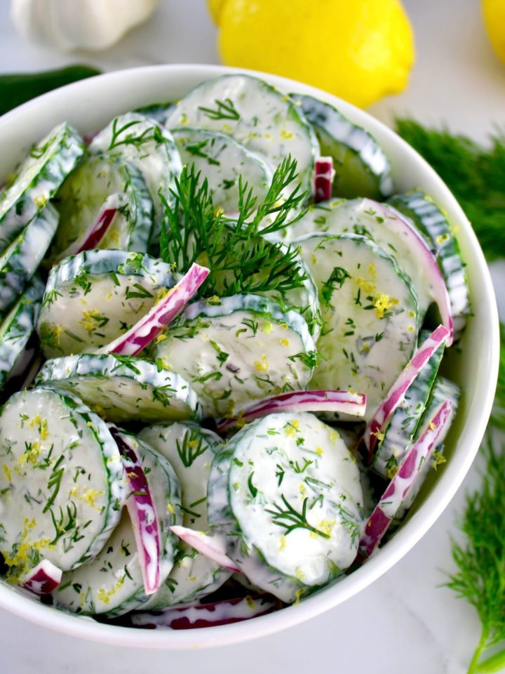 Creamy Cucumber Salad in white bowl with sprig of fresh dill