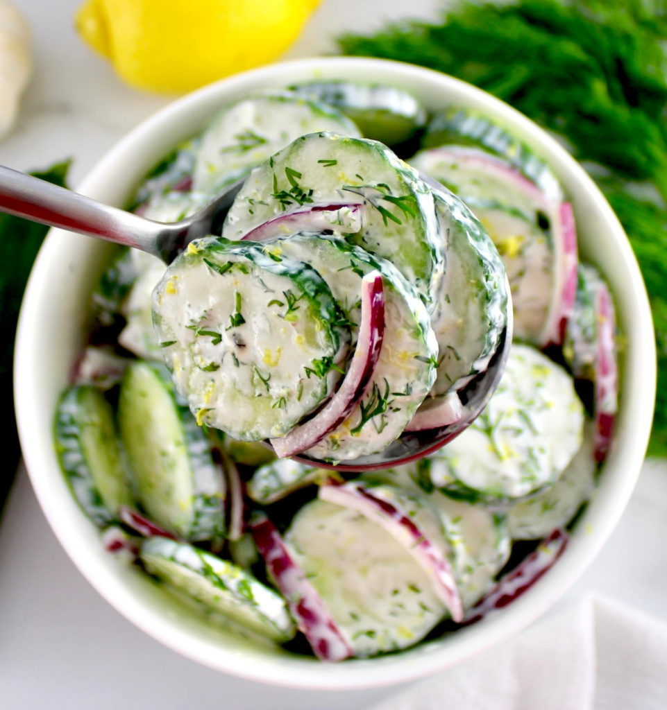 Creamy Cucumber Salad in spoon held up over bowl