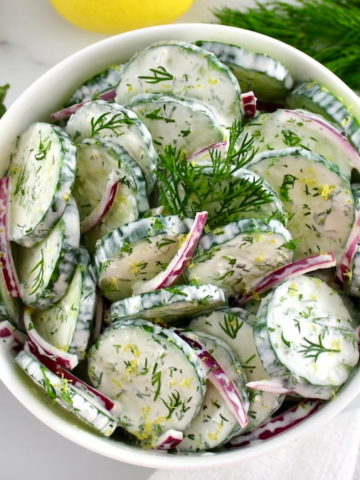 overhead view of Creamy Cucumber Salad in white bowl with fresh dill and cucumber on side