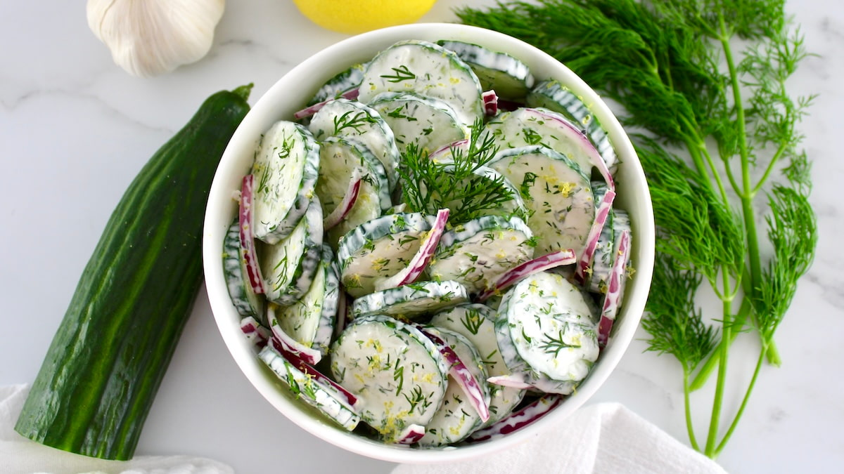 overhead view of Creamy Cucumber Salad in white bowl with fresh dill and cucumber on side
