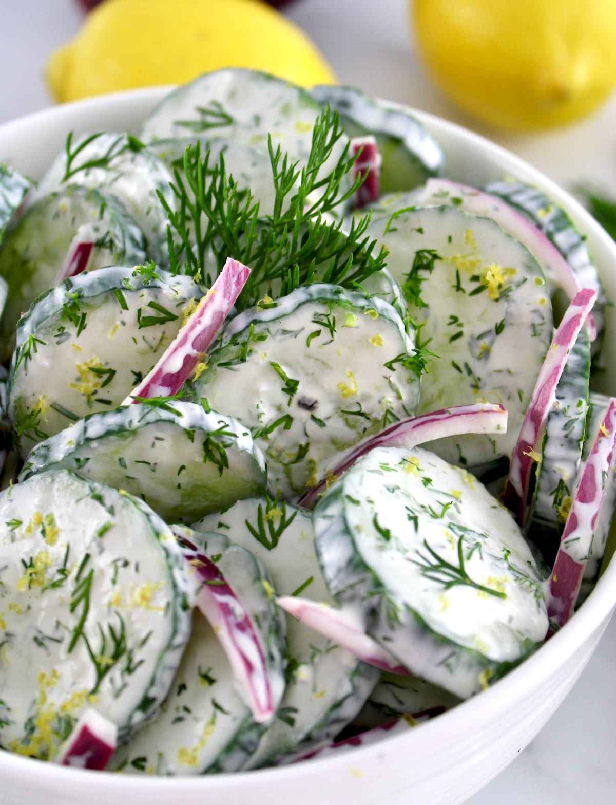 closeup of Creamy Cucumber Salad in white bowl with fresh dill