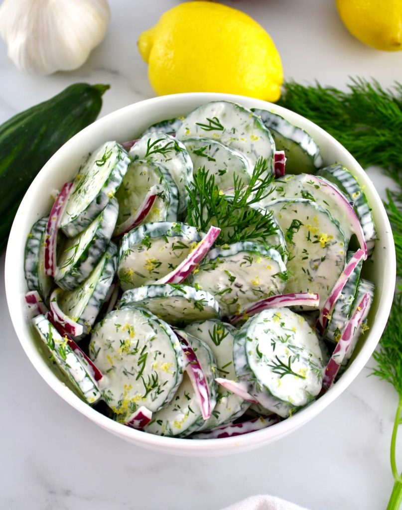 overhead view of Creamy Cucumber Salad with cucumber and lemon in back