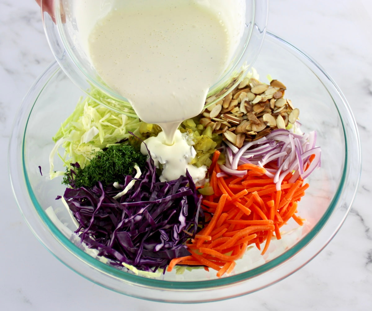 Dill Pickle Coleslaw ingredients in glass bowl in sections with dressing being poured over top