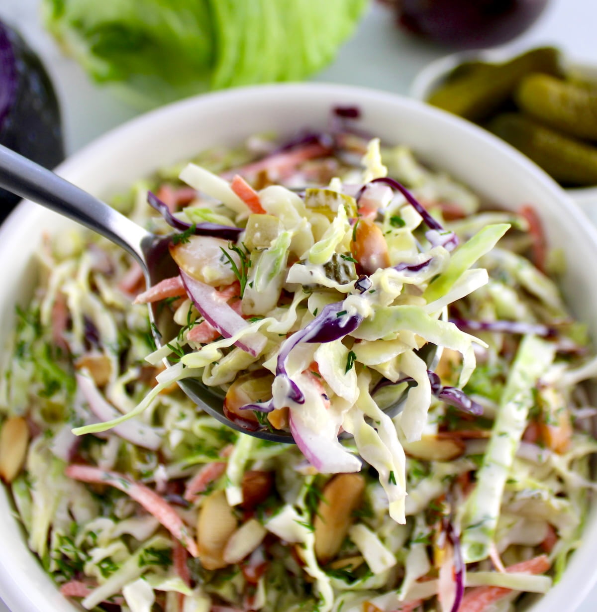 silver spoon holding up Dill Pickle Coleslaw over white bowl