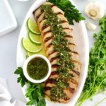Grilled Pork Tenderloin Chimichurri sliced on white platter with sauce in white cup and lime slices
