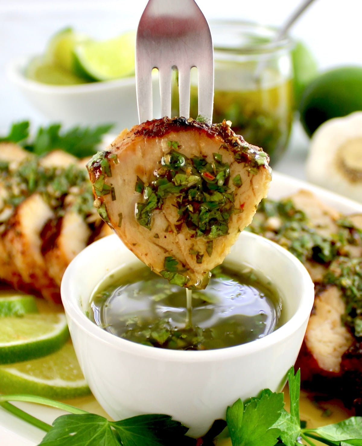 fork holding slice of Grilled Pork Tenderloin  dipped into Chimichurri sauce and dripping