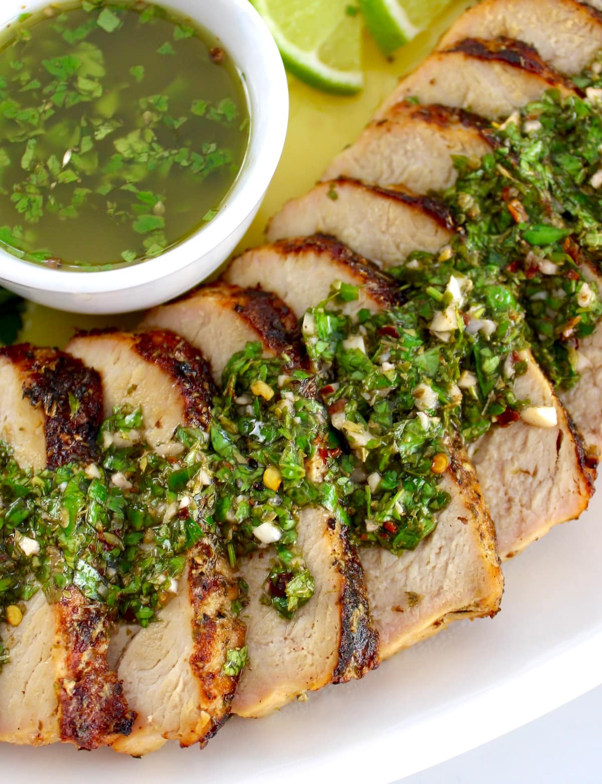 closeup of Grilled Pork Tenderloin  Chimichurri sliced on white plate with sauce in cup