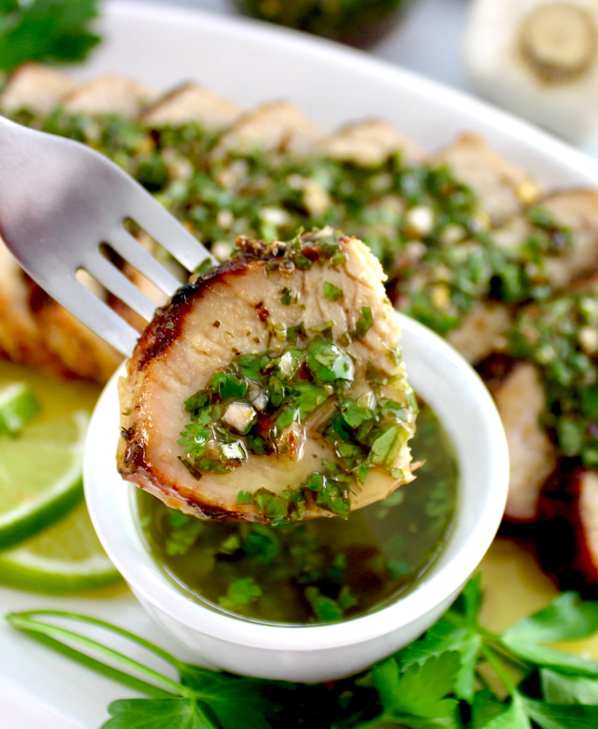 fork holding up slice of Grilled Pork Tenderloin dipped in Chimichurri sauce