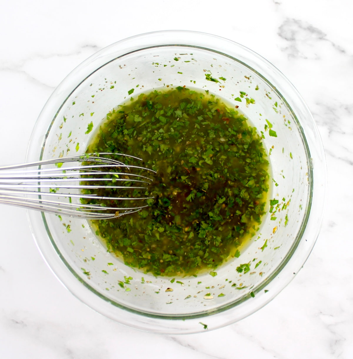 chimichurri sauce in glass bowl with whisk