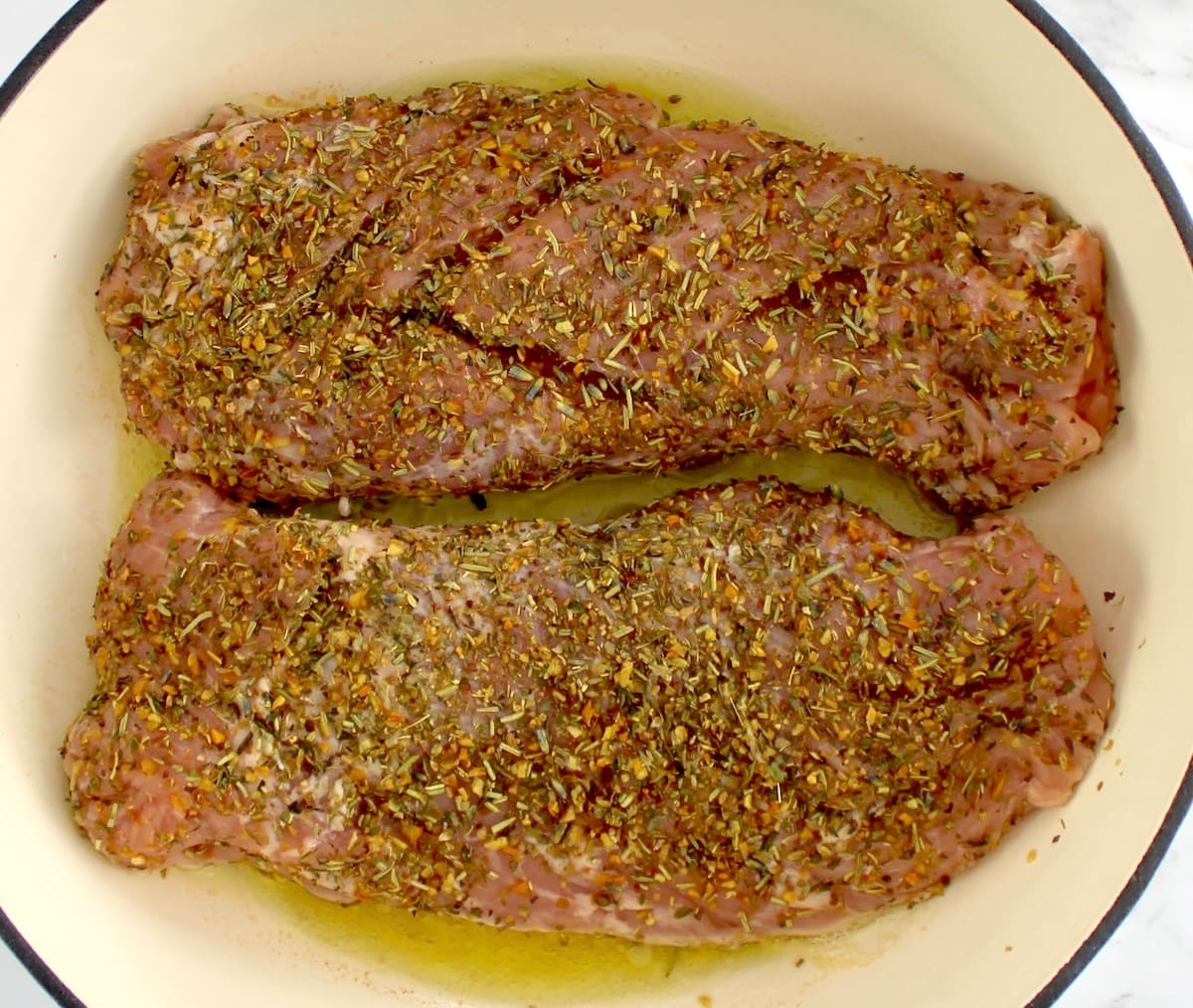 2 raw pork tenderloins with herb rub in pan