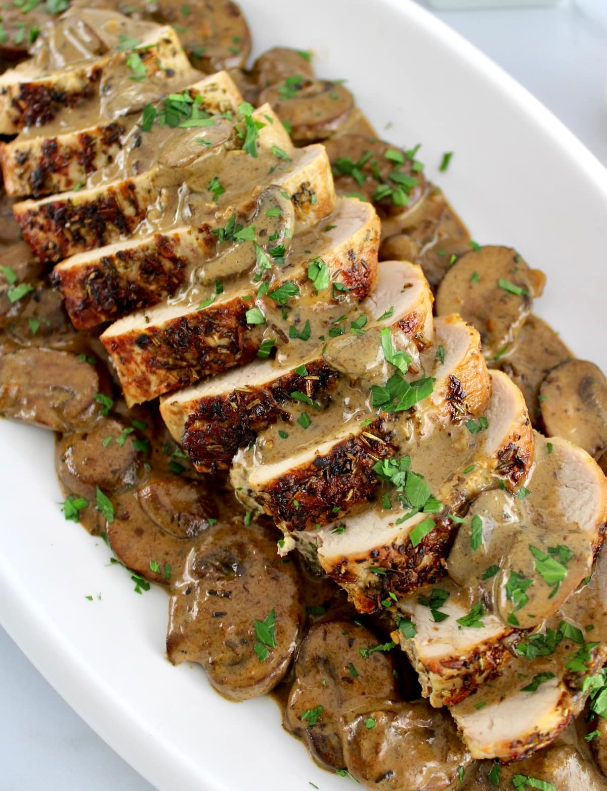 sliced Herb Crusted Pork Tenderloin with Mushroom Gravy on white plate with chopped parsley