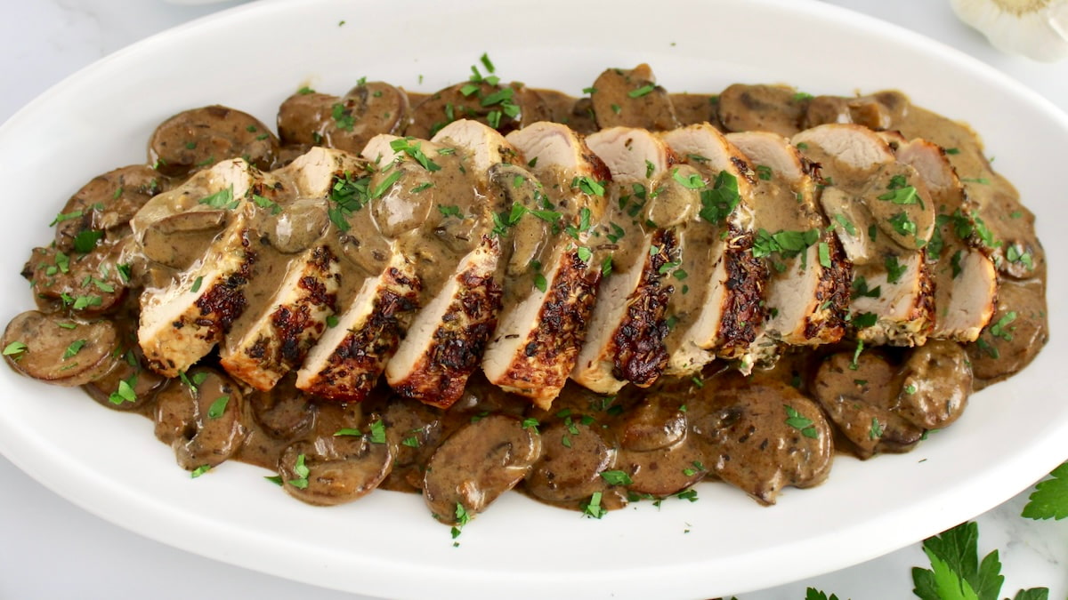 Herb Crusted Pork Tenderloin with Mushroom Gravy sliced on white oval platter
