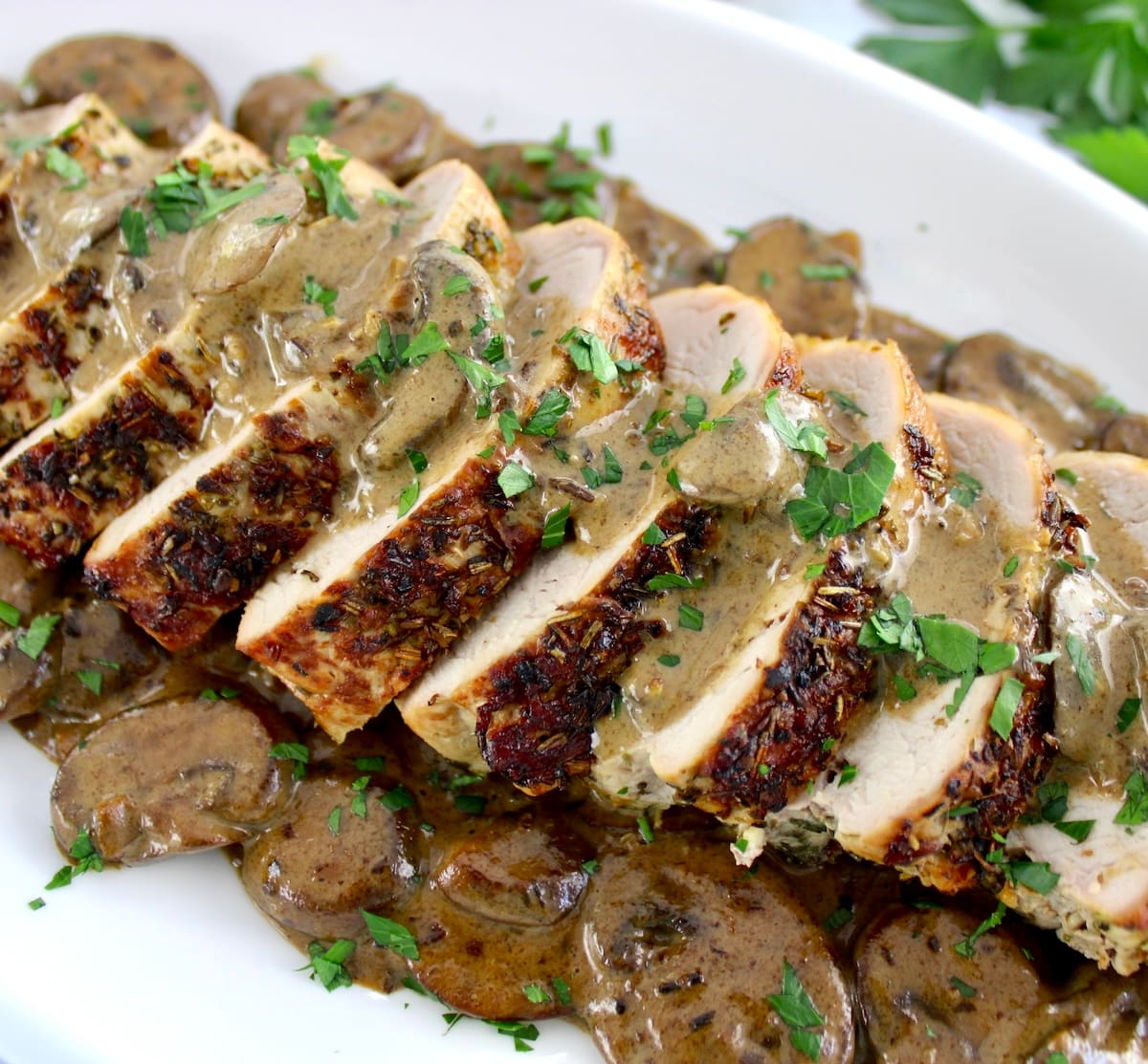 closeup of sliced Herb Crusted Pork Tenderloin with Mushroom Gravy on white dish