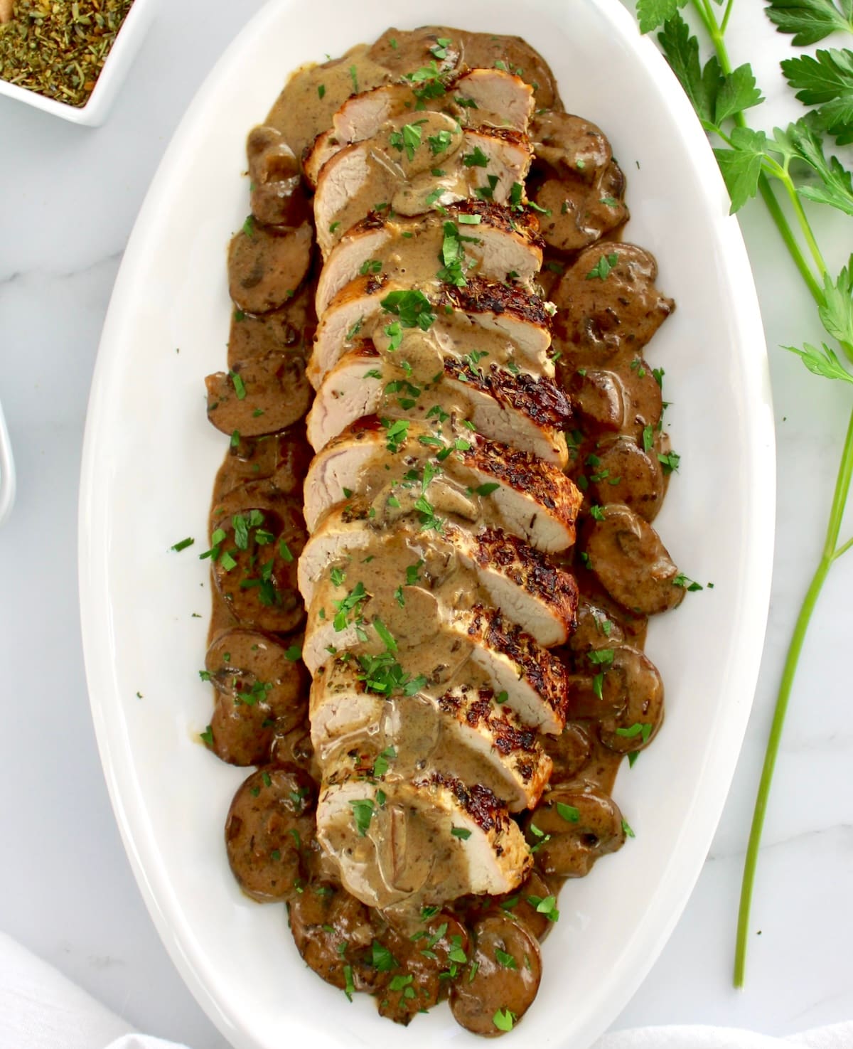 overhead view of Herb Crusted Pork Tenderloin with Mushroom Gravy sliced on white oval platter