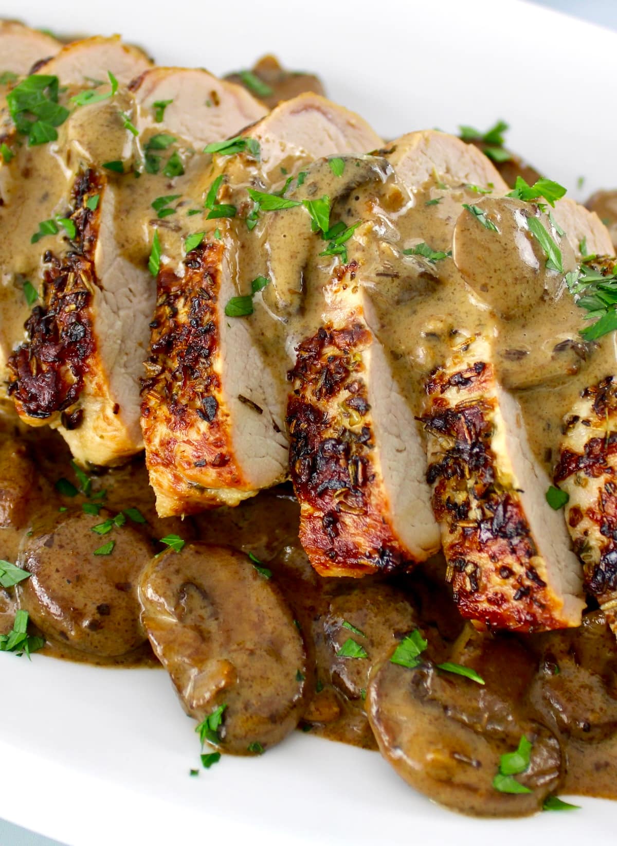 closeup of sliced Herb Crusted Pork Tenderloin with Mushroom Gravy on white plate