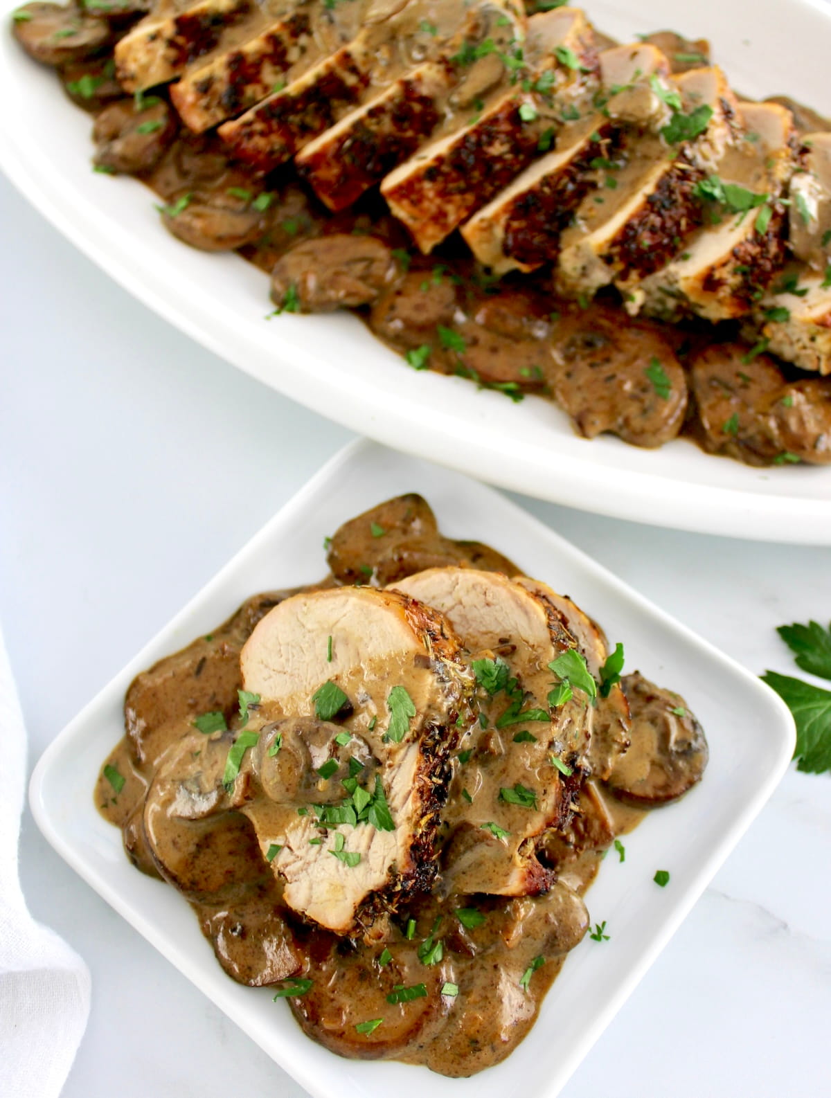 sliced Herb Crusted Pork Tenderloin with Mushroom Gravy on white plate with more on white platter in back