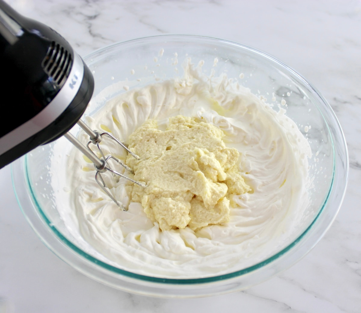 whip cream and mascarpone being mixed together in glass bowl with hand mixer