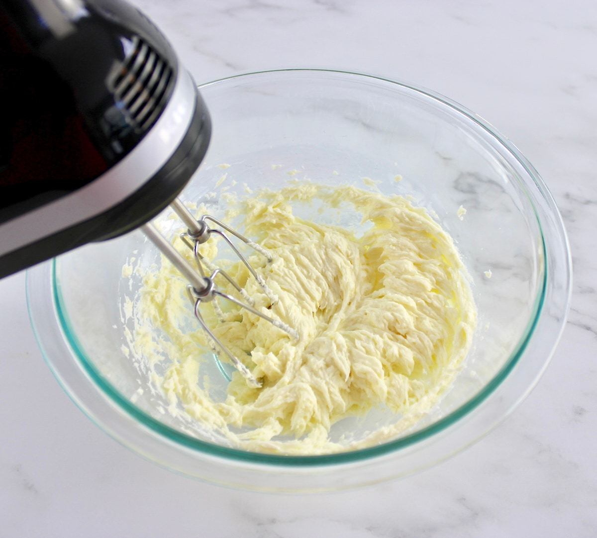 mascarpone cheese being whipped in glass bowl with hand mixer