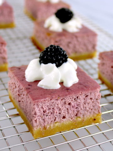 closeup of Blackberry Cheesecake Bar on wire rack with whip cream and blackberry on top