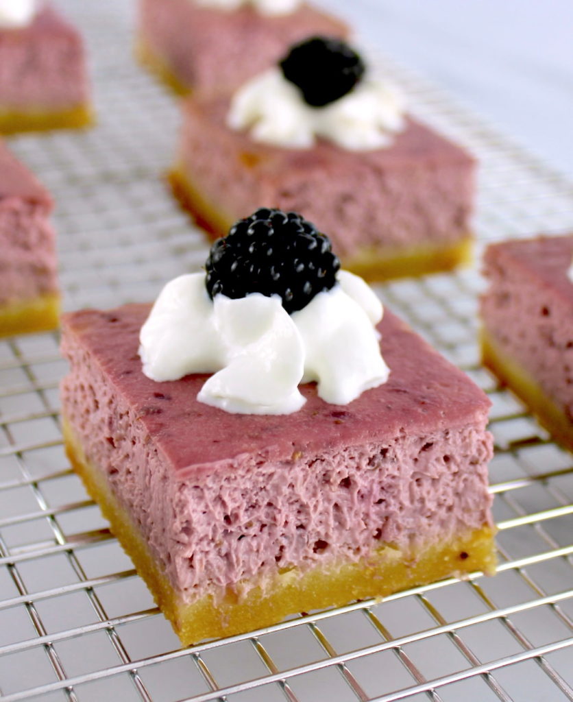 closeup of Blackberry Cheesecake Bar on wire rack with whip cream and blackberry on top