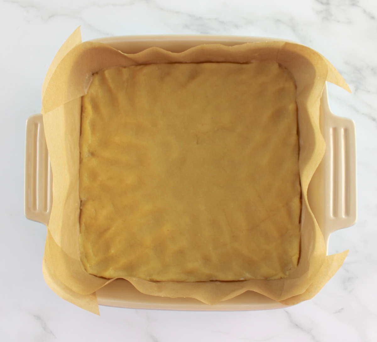 Blackberry Cheesecake Bars crust in baking dish with parchment paper