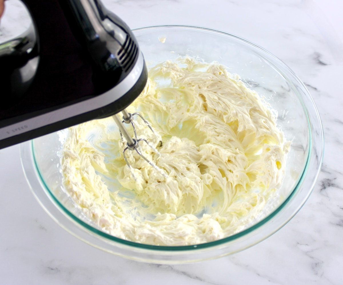 cream cheese and sour cream being mixed with hand mixer