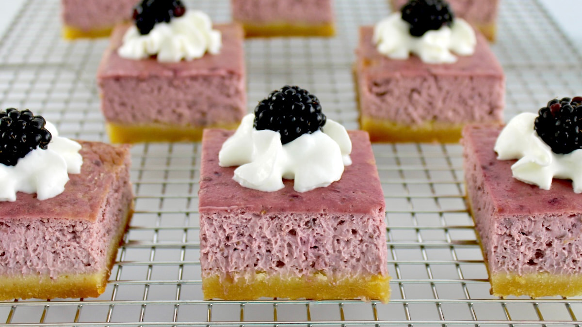 Blackberry Cheesecake Bars on cooling rack with whip cream and blackberries on top