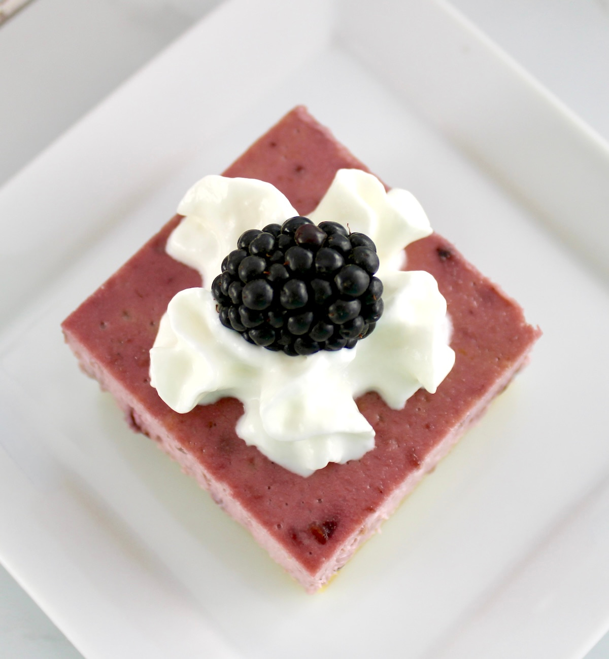 overhead view of Blackberry Cheesecake Bar on white plate with whip cream and blackberry on top