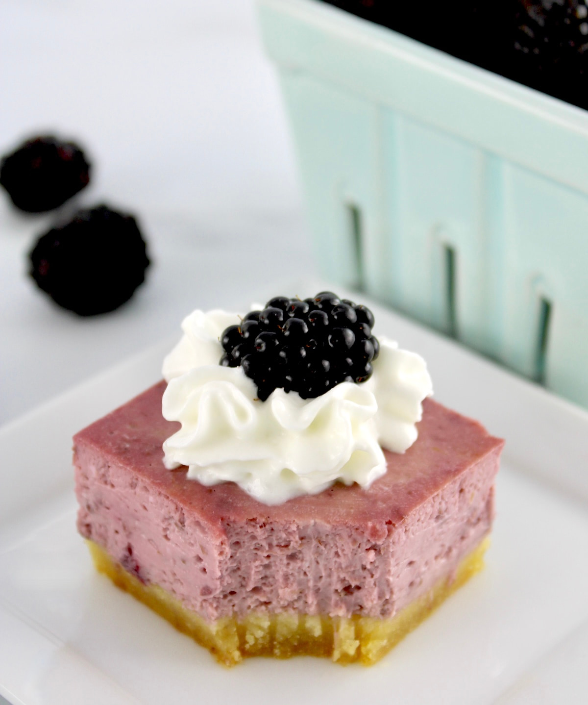 Blackberry Cheesecake Bar on white plate with bite missing and whip cream and blackberry on top