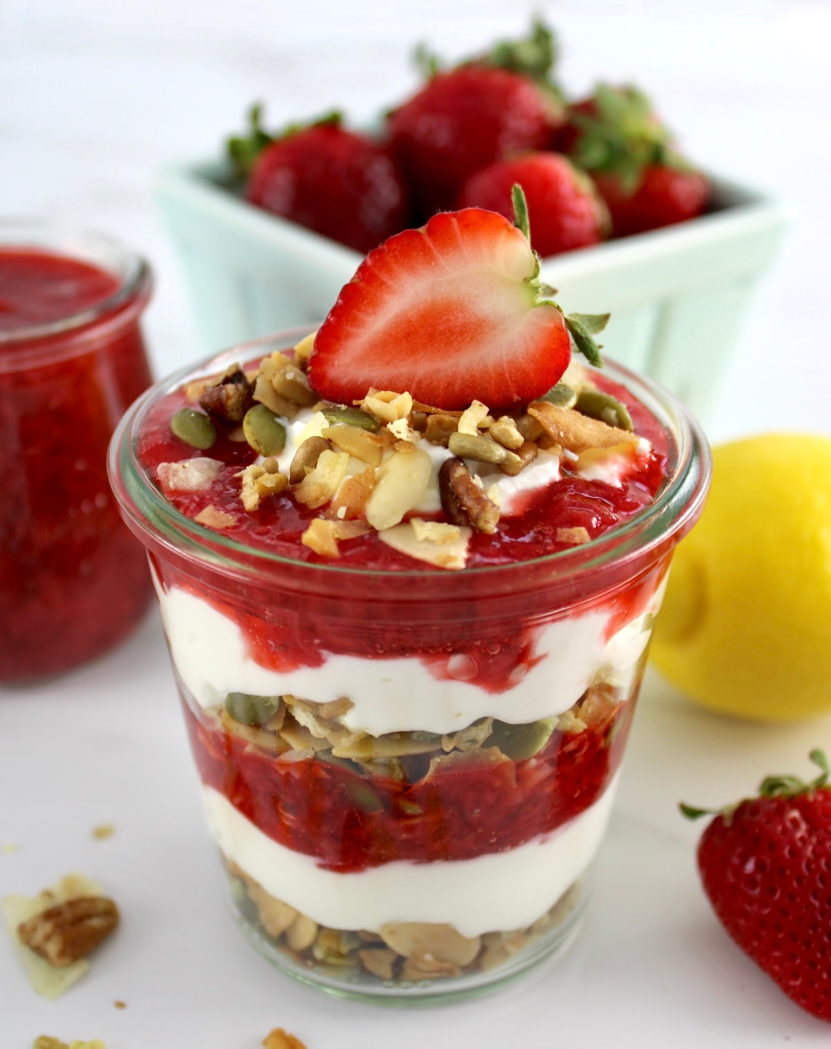 Keto Strawberry Granola Parfait in open glass jar with half strawberry on top and strawberries in back
