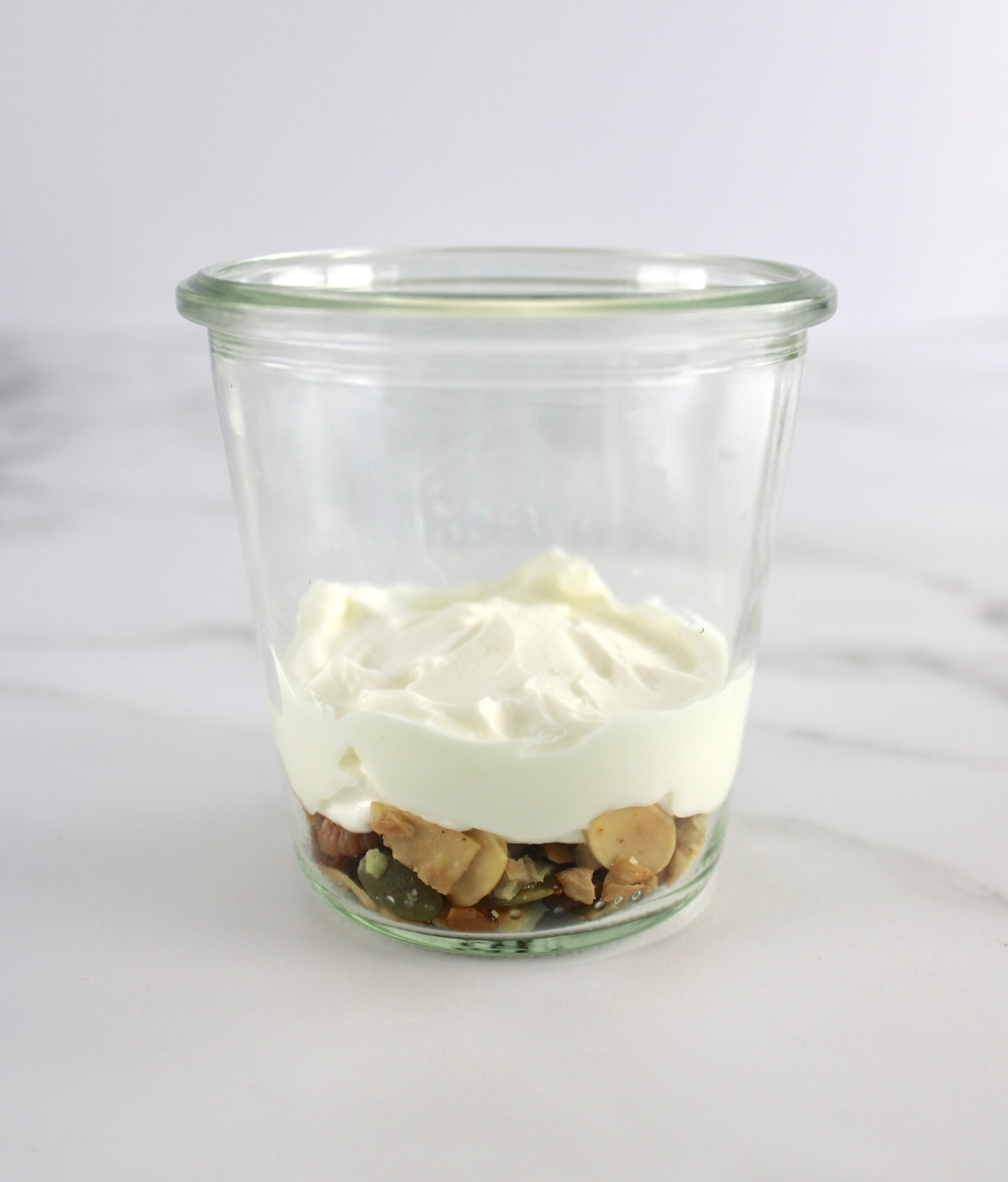 side view of open glass jar with keto granola and Greek yogurt on bottom