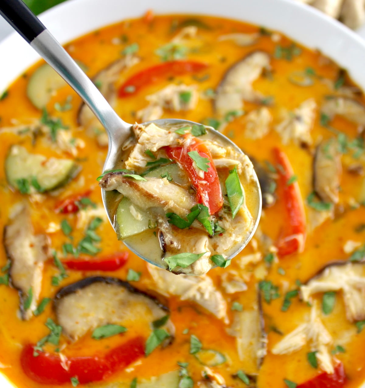 spoonful of Thai Coconut Curry Chicken Soup held up over white bowl
