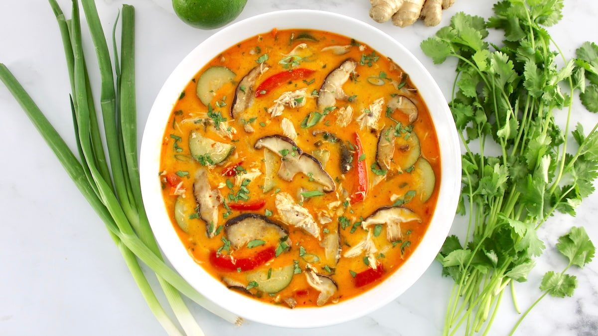 overhead view of Thai Coconut Curry Chicken Soup in white bowl with fresh cilantro and veggies around