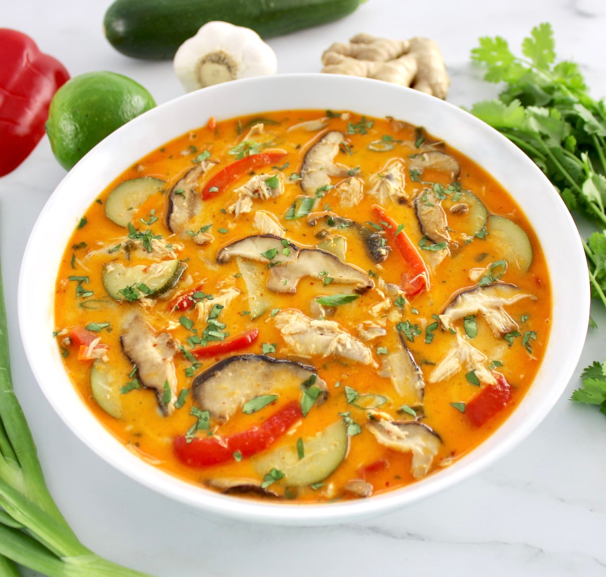 closeup of Thai Coconut Curry Chicken Soup in white bowl with veggies in back