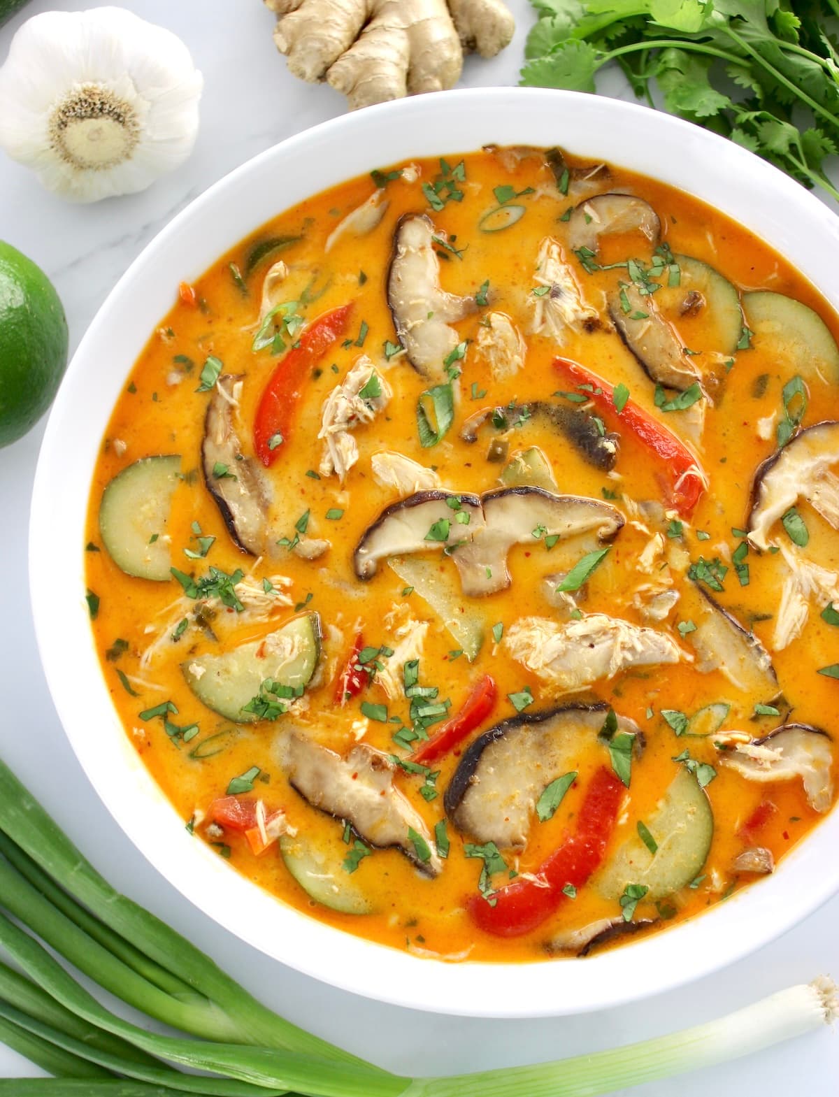 overhead view of Thai Coconut Curry Chicken Soup in white bowl with fresh cilantro and veggies around