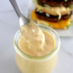 Keto Big Mac Sauce being spooned out of open glass jar with burger in back