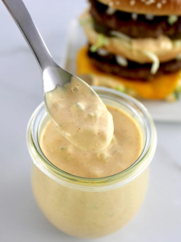 Keto Big Mac Sauce being spooned out of open glass jar with burger in back