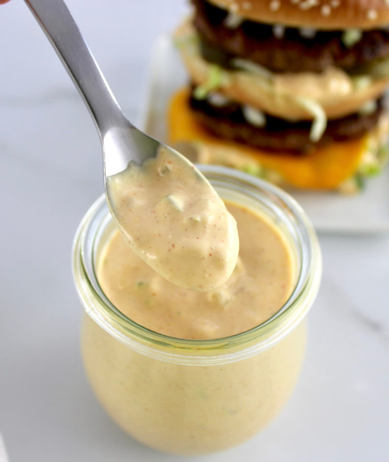 Keto Big Mac Sauce being spooned out of open glass jar with burger in back