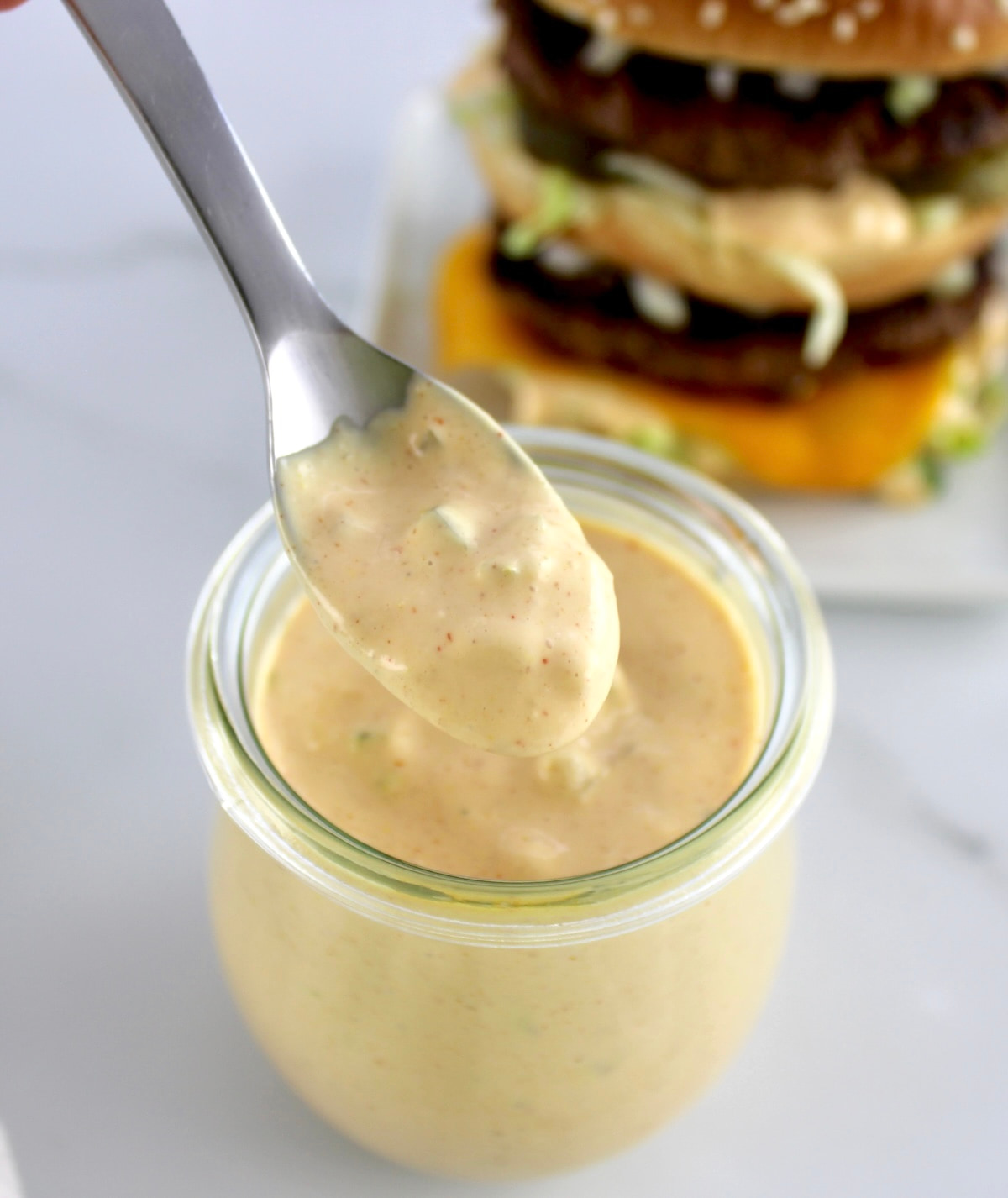 Keto Big Mac Sauce being spooned out of open glass jar with burger in back
