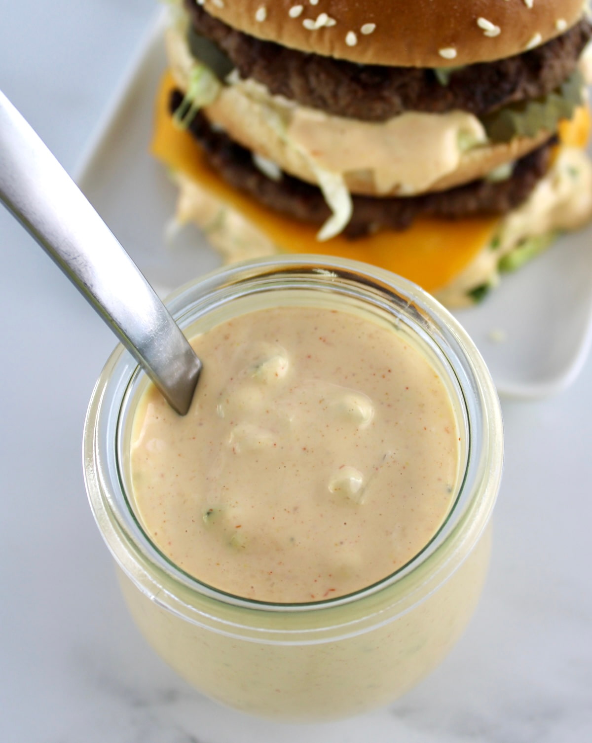 overhead view of Keto Big Mac Sauce in open jar with spoon it in and burger in back
