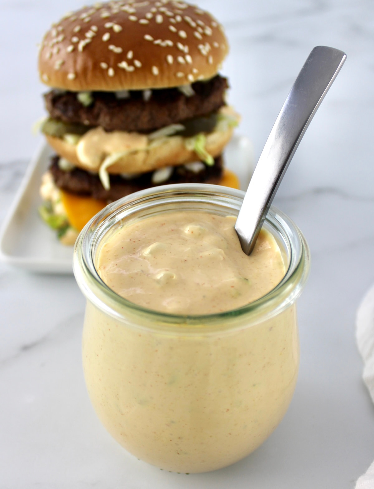 Keto Big Mac Sauce in open glass jar with spoon and burger in back